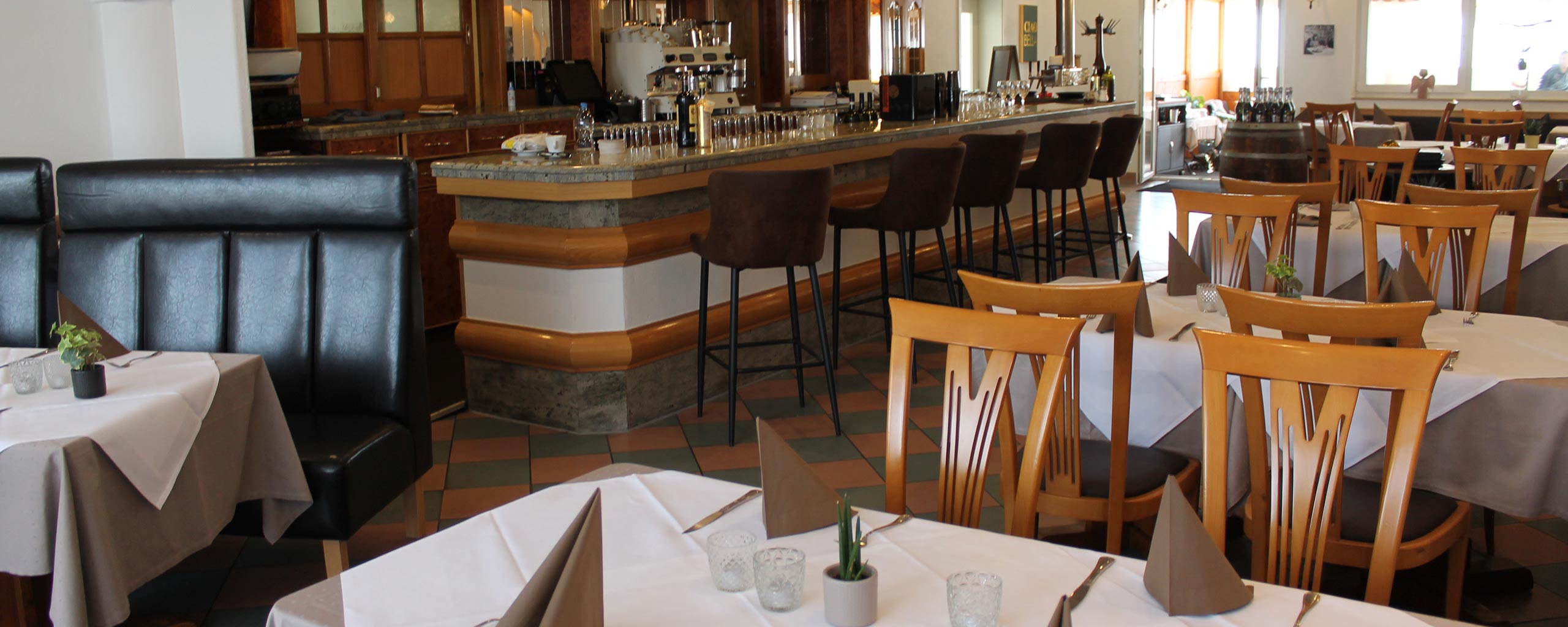 Restaurant Il Caminetto mit eingedeckten Tischen, Stoffservietten und Holzstühlen, im Hintergrund die Bar mit Barhockern
