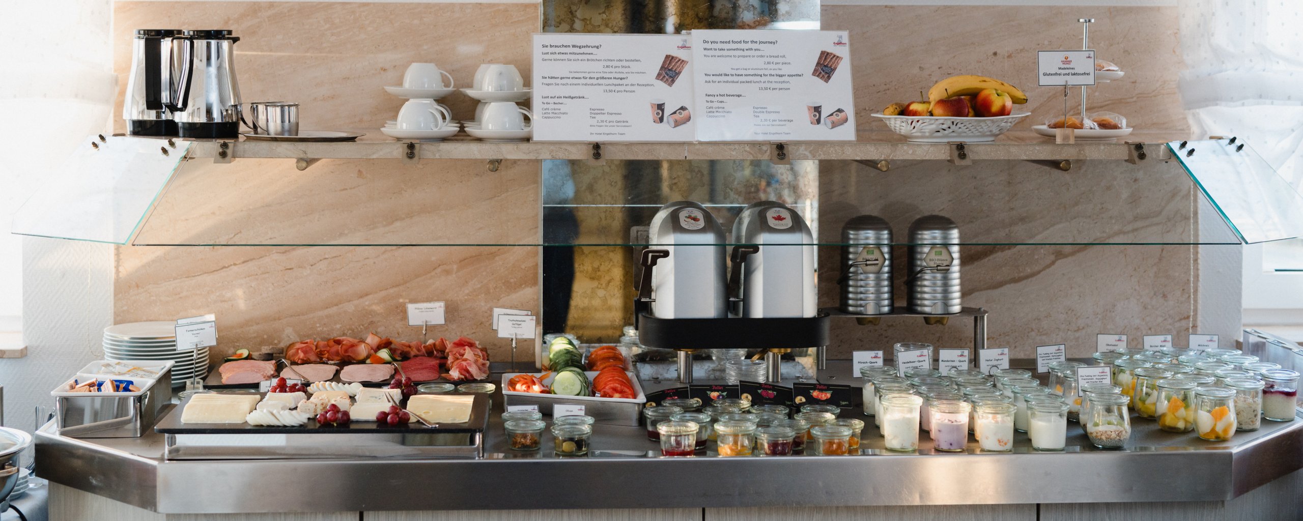 Frühstücksbuffet in voller Breite: Aufschnitt, Käse, Gemüse, Weckgläser mit Quark und Obst, dahinter Kaffeeautomaten