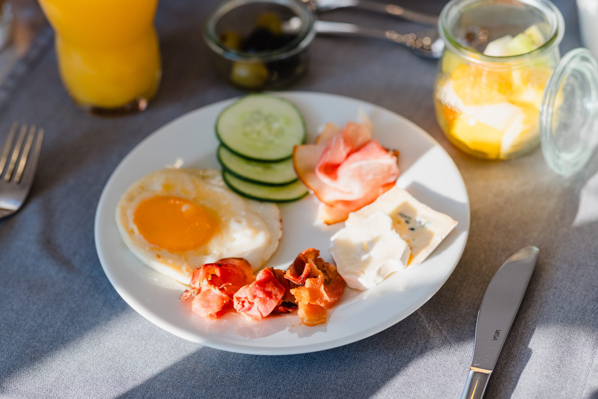 Teller mit Spiegelei, Lachs, Gurke und Käse auf dem sonnigen Frühstückstisch